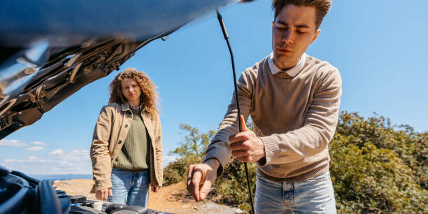Young man looking under the hood of a broken car.